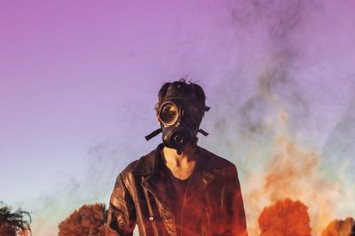 Man wearing gas mask while standing against sky during sunset