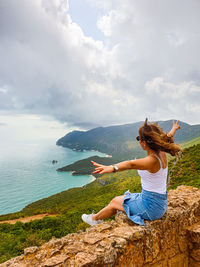 Woman by sea against sky. she is afraid of height but sits on the edge