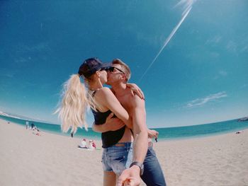 Low angle view of couple kissing at beach against sky during sunny day