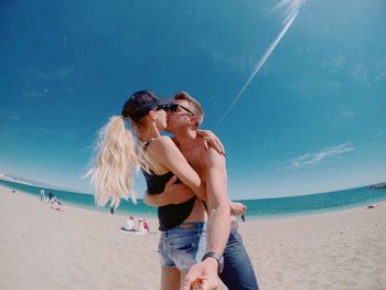 Happy friends standing on beach against sky