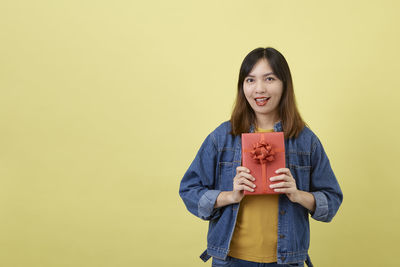 Portrait of smiling young woman against yellow background