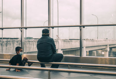 Rear view of man sitting near glass window