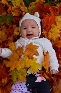 Portrait of cute baby girl lying amidst autumn leaves