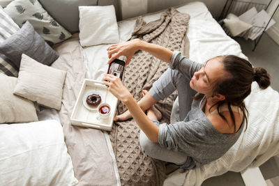 Woman taking shot of tray with food on bed