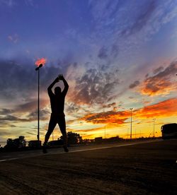 Silhouette man standing by road against sky during sunset