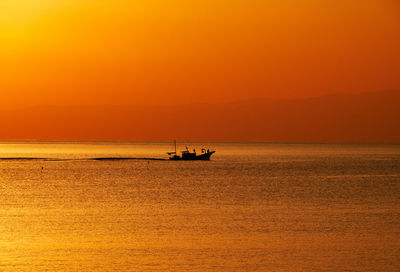 Silhouette boat in sea against orange sky