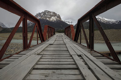 Wooden road bridge crosses river with view of andes mountains, near el chalten, patagonia, argentina