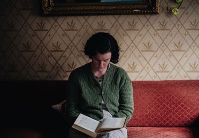 Young woman reading book while sitting on sofa at home