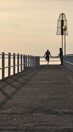 Man walking on footpath by pier against sky during sunset