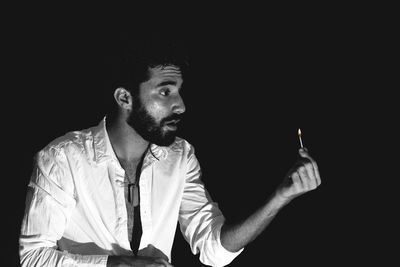 Young man holding matchstick against black background