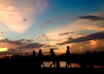 Silhouette people by sea against sky during sunset