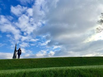 Low angle view of young woman standing on grassy field against cloudy sky