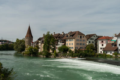 Buildings by river against sky