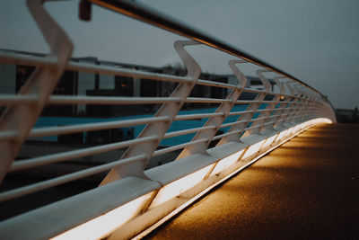 Close-up of metallic chair by railing against sky