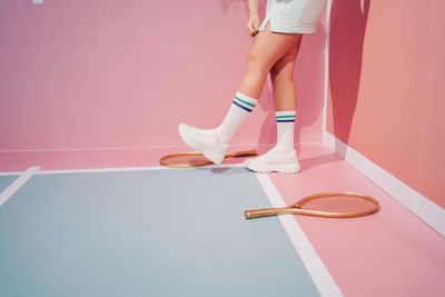 Side view of crop unrecognizable stylish female athlete in knee socks with tennis racket walking on sports ground