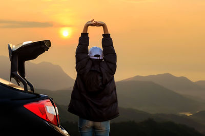 Rear view of man on car against mountains during sunset