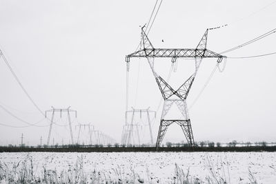 Electricity pylon on field against sky in winter