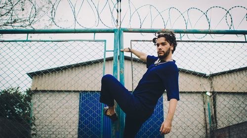 Side view of man sitting on chainlink fence