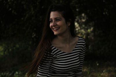 Smiling young woman looking away against tree