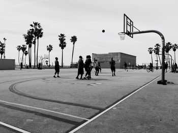 Friends playing basket ball at court against clear sky