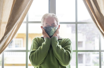 Portrait of senior man wearing mask standing against wall at home