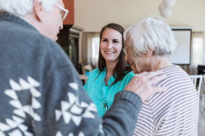 Smiling young female nurse looking at senior couple in nursing home