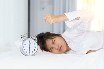 Woman looking at alarm clock on bed at home