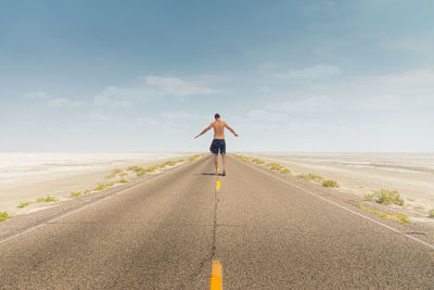 Rear view of shirtless man walking on road at beach against sky