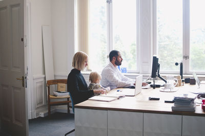 Working mother with daughter sitting by male colleague in office