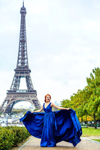 Portrait of smiling young woman tower against cloudy sky