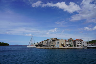 Sailboats in sea by buildings against sky