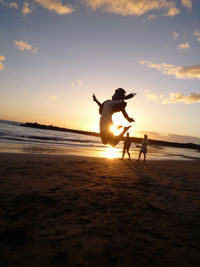 Silhouette men on beach against sky during sunset