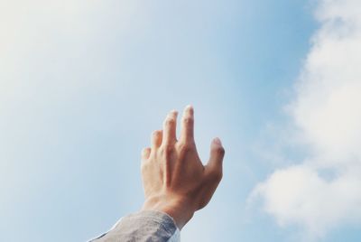 Low angle view of cropped hand against sky