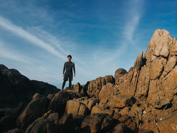 Low angle view of man standing on rock formation against sky