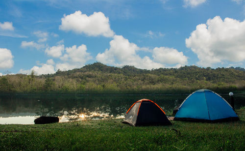 Tent on field by lake against sky