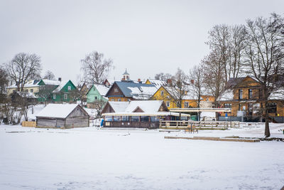 Houses on snow covered field by building against sky