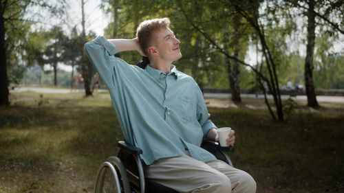 Young man on wheelchair holding glass sitting at park