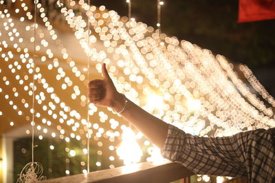 Close-up of man showing thumbs up against illuminated lighting equipment at night