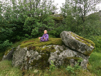 Girl doing yoga while sitting on rock at forest