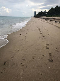 Footprints on sand at beach against sky