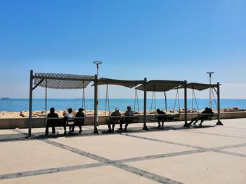 People sitting on beach against clear sky