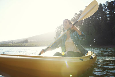 Smiling woman looking away while kayaking on lake against sky during sunny day
