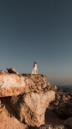 Woman sitting on rock by sea against clear sky