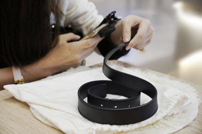 Woman using a magnifying glass to check the authenticity of a leather belt