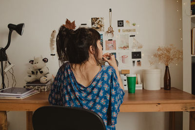 Rear view of woman using mobile phone while sitting at home