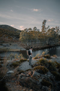 Side view of man standing on rock at lakeshore against sky