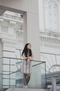 Young woman looking away while standing by railing against building 