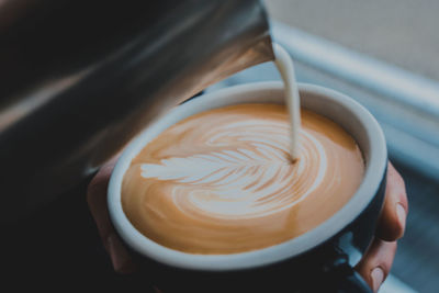 Close-up of hands making froth art coffee on table