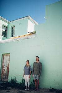 Full length portrait of young couple standing against house