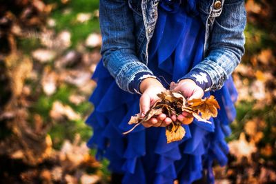 Midsection of girl holding leaves while standing on field